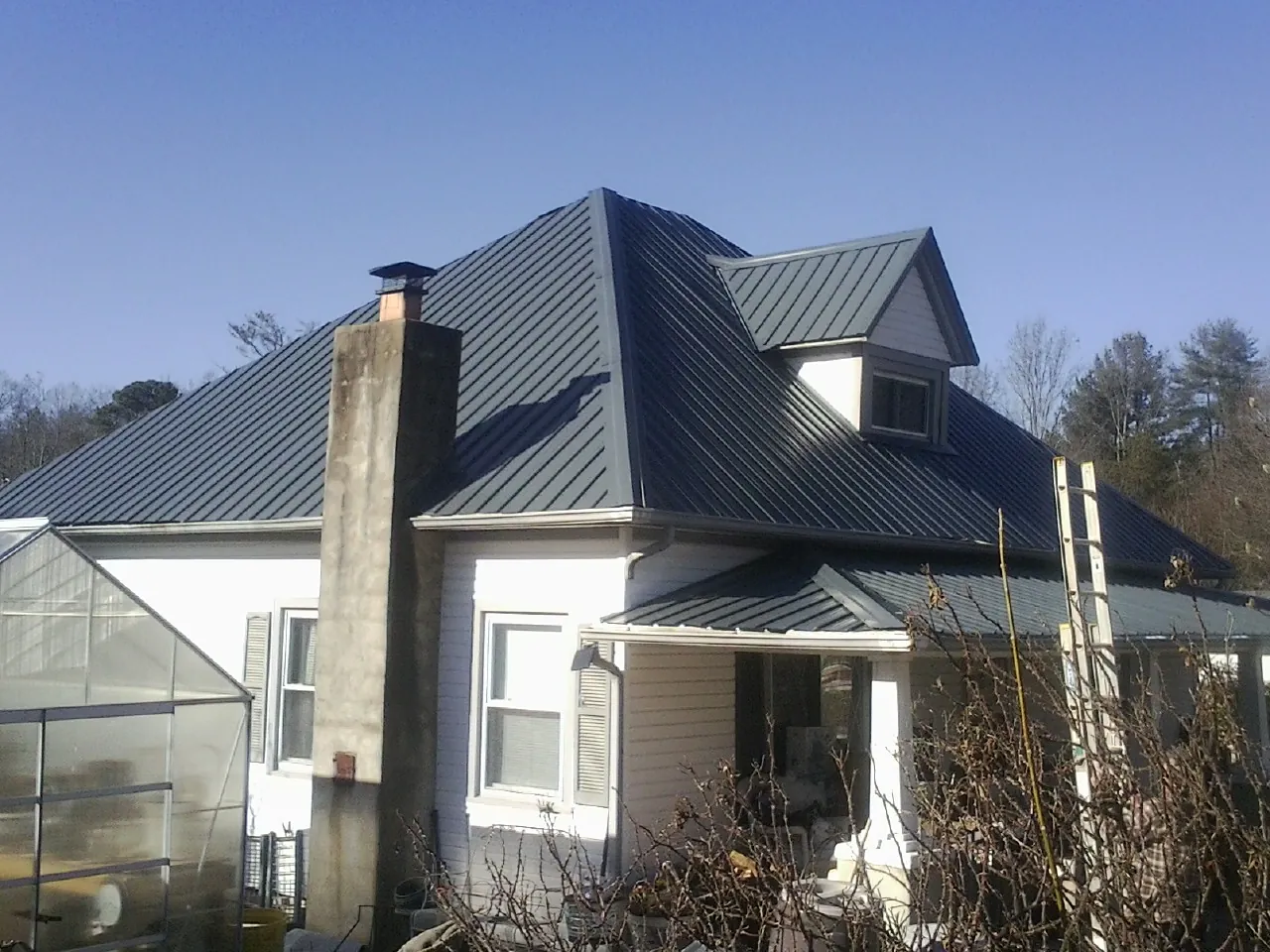 Dark blue standing seam metal roof on a white farmhouse with dormer — Slate & Tile Roof Repair by Roofing Brothers in Blowing Rock