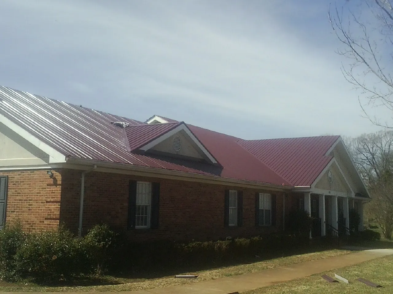 Red metal roof with gabled entries on a long brick building, from a Hail Damage Roof Repair job in Blowing Rock