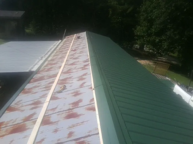 Old rusted panels beside newly installed green metal roofing — Wind Damage Roof Repair by Roofing Brothers in Blowing Rock