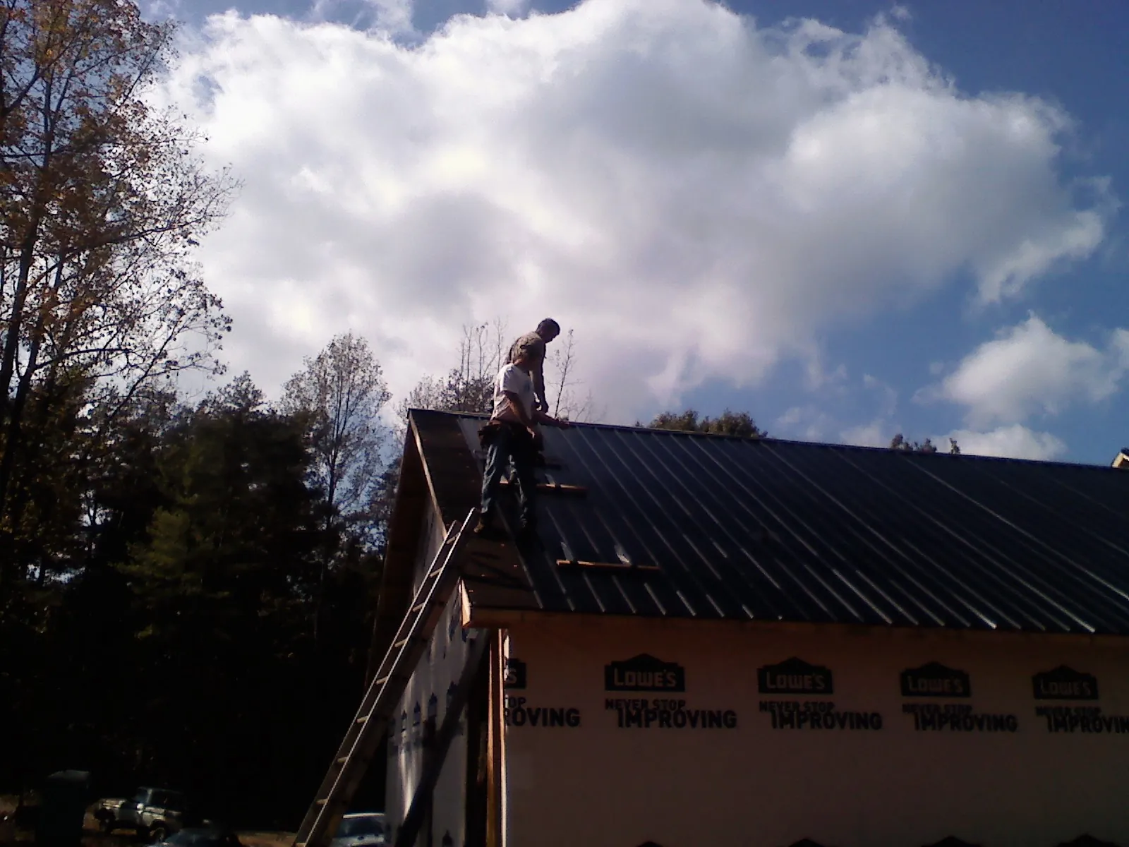 Roofer fastening dark metal panels high against a cloudy sky, from a Roof Inspection job in Blowing Rock