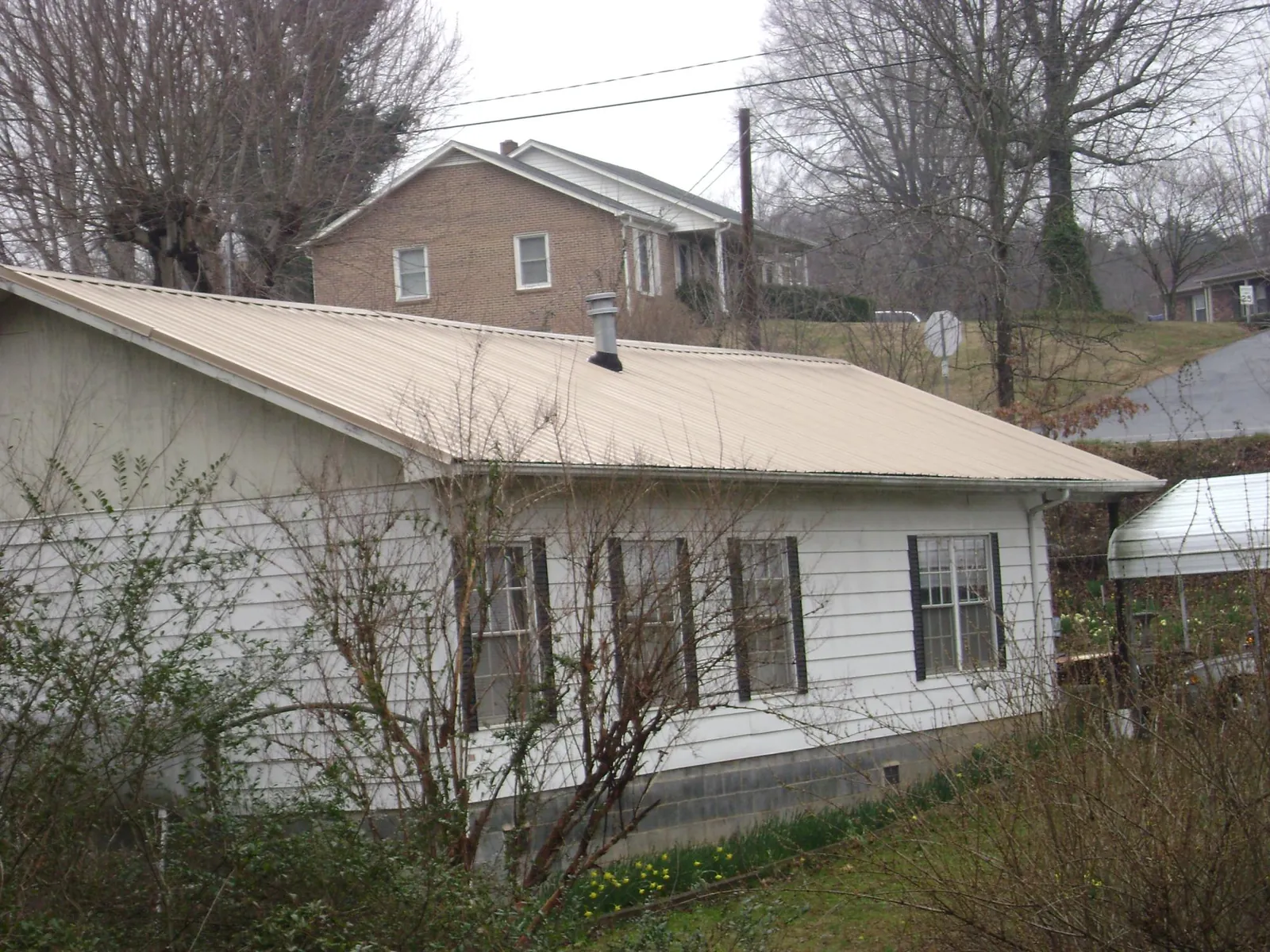 Tan metal roof on a white sided house set into a hillside — Commercial Roofing by Roofing Brothers in Blowing Rock