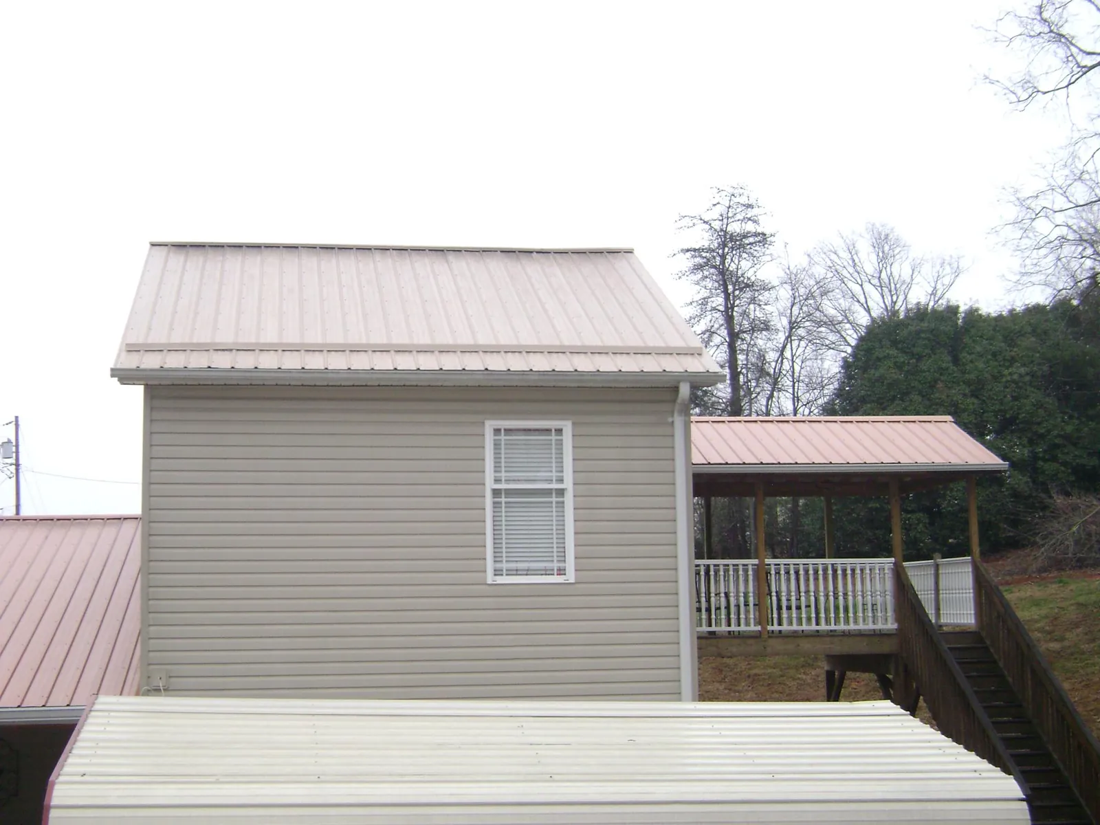 Tan metal roofs on a two story addition and attached porch, from a Roof Replacement job in Blowing Rock