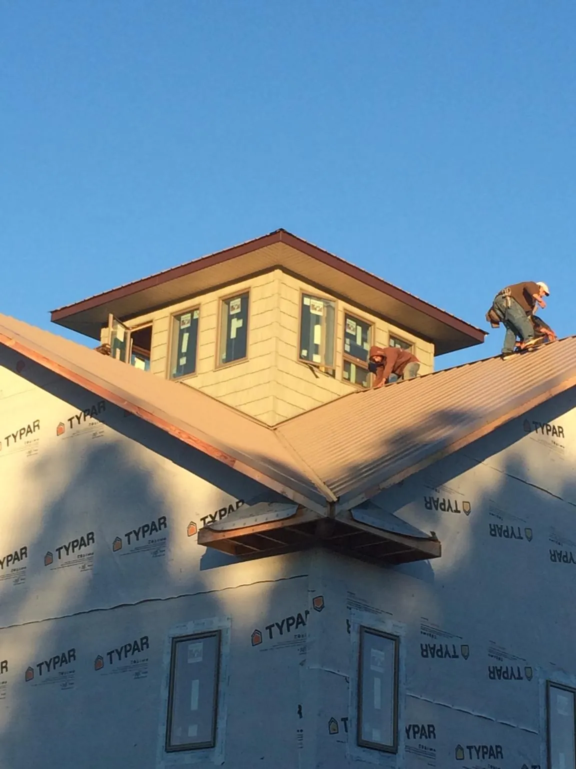 Roofers working around a rooftop cupola on a new metal roof at sunset — Roof Waterproofing in Blowing Rock by Roofing Brothers